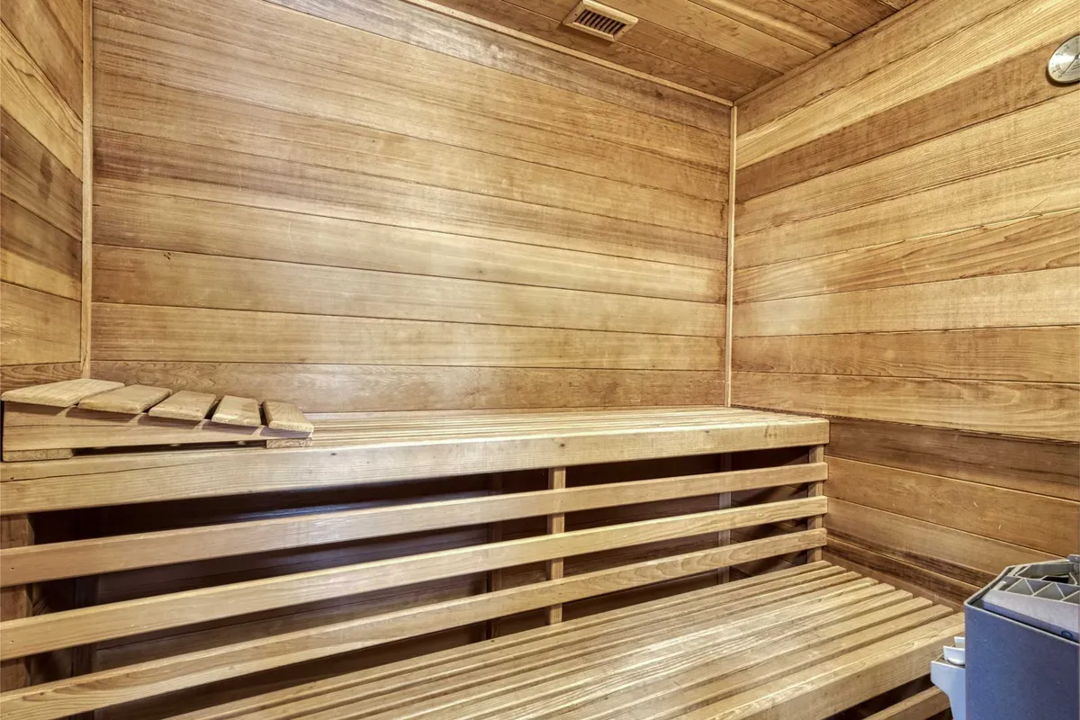 A tranquil interior scene of a wooden sauna, with warm lighting, wooden benches, and walls that evoke a classic, restorative sauna experience. The atmosphere is peaceful, suggesting moments of solitude or shared wellness routines.