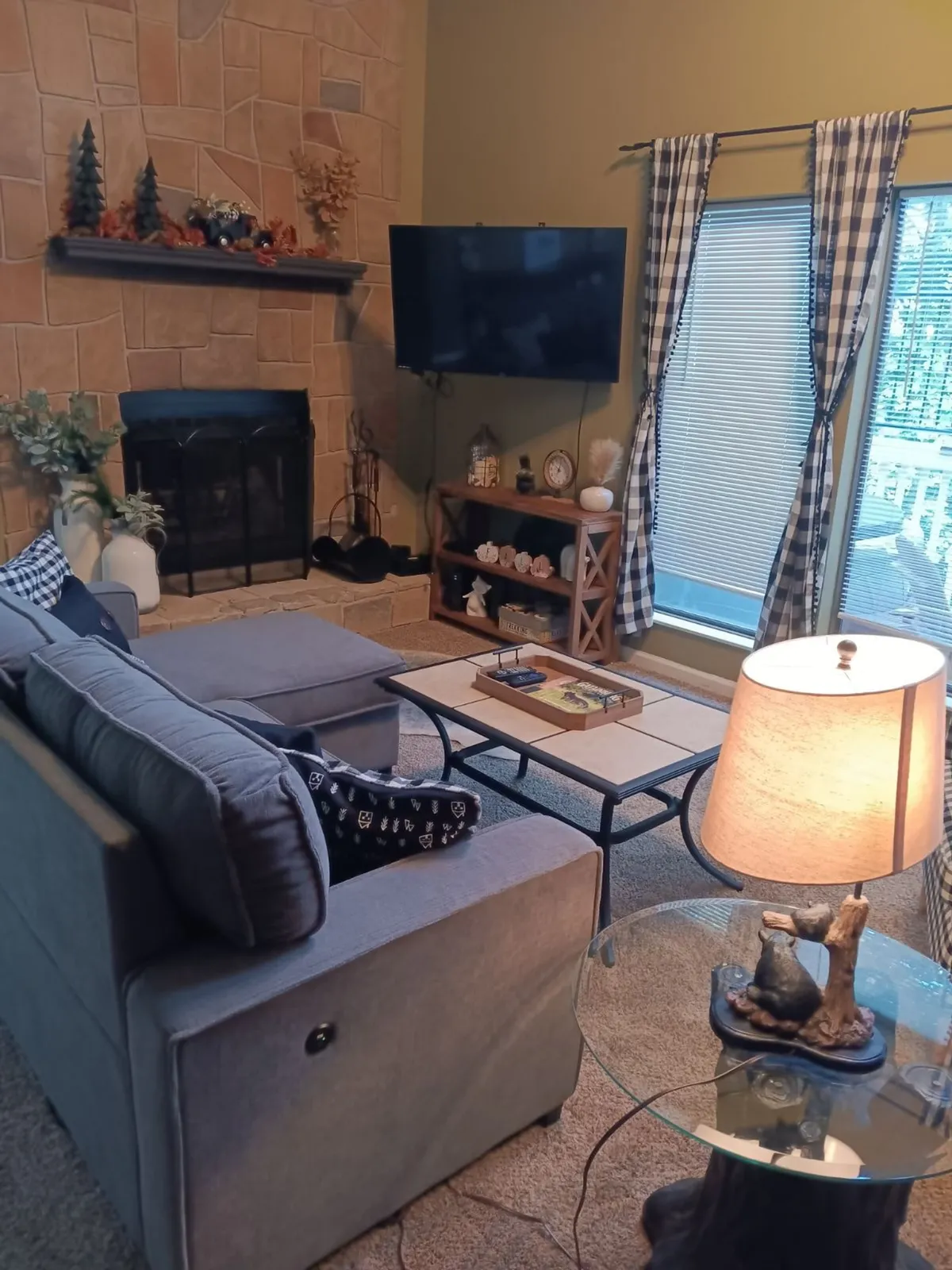 An interior living space featuring a comfortable sofa, accent chairs, a coffee table, and a prominent fireplace. Thoughtful décor, soft lighting from a lamp, and large windows contribute to the cozy, elegant mountain atmosphere described in the section.