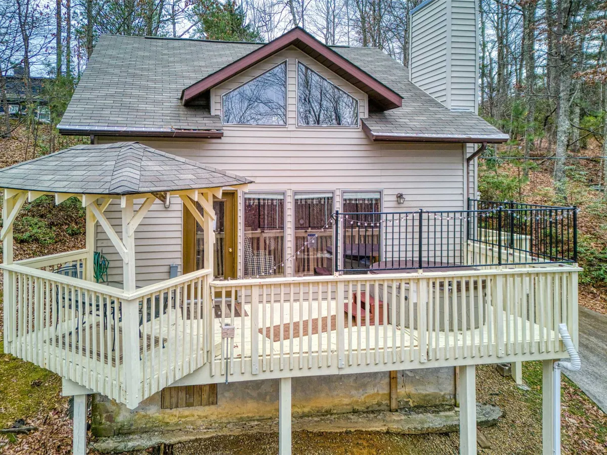 An inviting view of the chalet’s exterior shows a spacious deck with seating, large windows, and a roofline framed by mature trees. The scene suggests cozy evenings and the opportunity to enjoy sunset views or morning coffee in a private, natural setting.