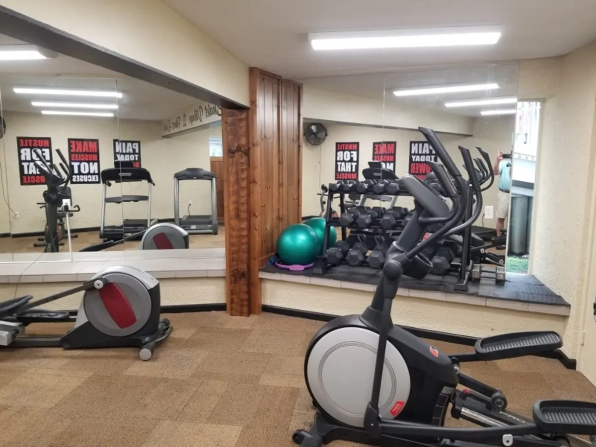 A bright and energetic gym interior featuring an elliptical machine, treadmill, weights, an exercise ball, and mirrors. The space feels modern, with ample equipment for a variety of workouts, inviting guests to pursue their fitness goals.