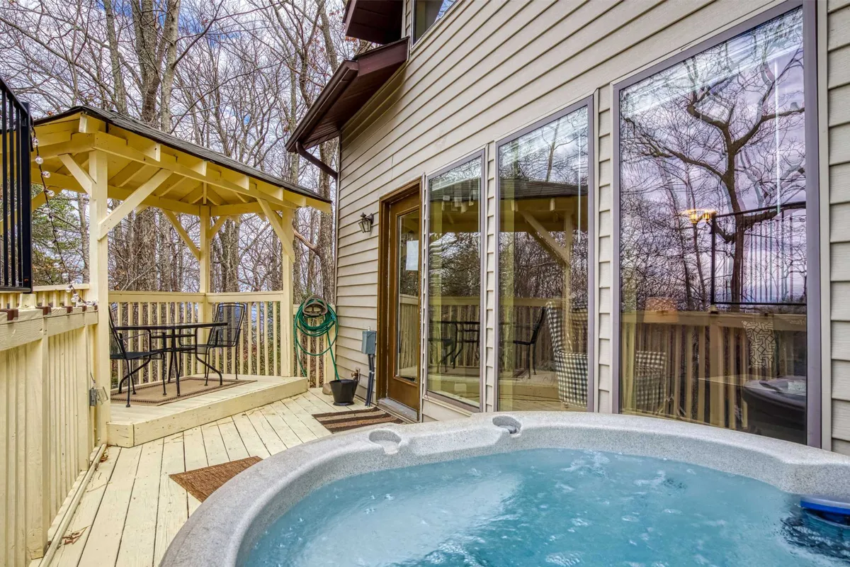 An exterior shot of a spacious hot tub set beneath a covered gazebo, surrounded by a deck area and lush greenery. The scene radiates calm, with inviting seating and glimpses of nature all around. It's easy to imagine relaxing in the warm water while soaking in serene mountain views.