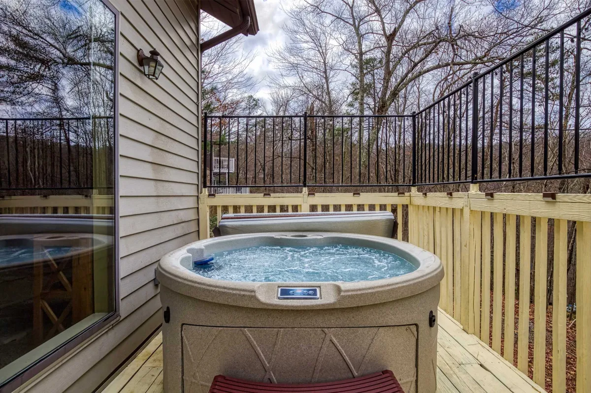 This exterior shot captures a hot tub nestled on a wooden deck, surrounded by lush trees, offering a tranquil and secluded atmosphere. The scene radiates privacy and relaxation, ideal for couples returning from mountain adventures to unwind under the stars or with morning coffee.