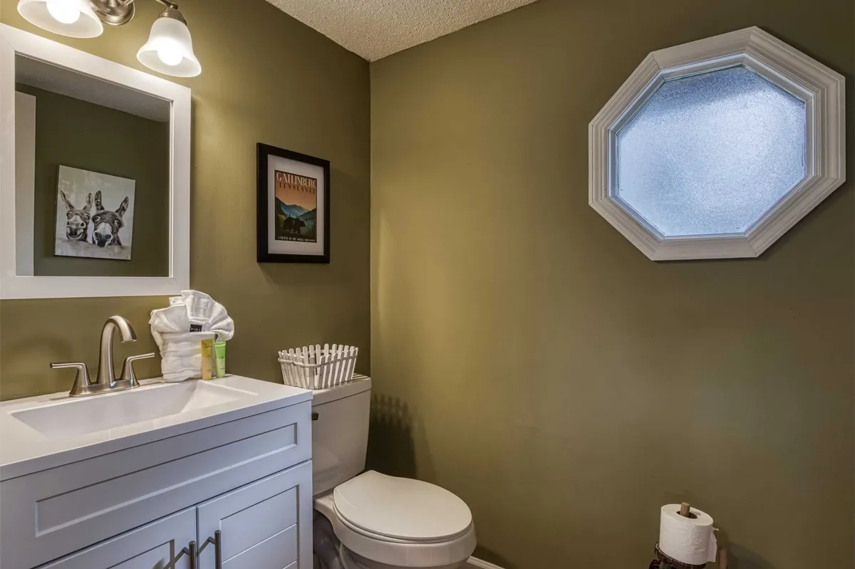 A neat half bath with a vanity sink, octagonal window providing natural light, and tasteful framed artwork. The calm and tidy design offers a peaceful nook for quick grooming and freshening up.