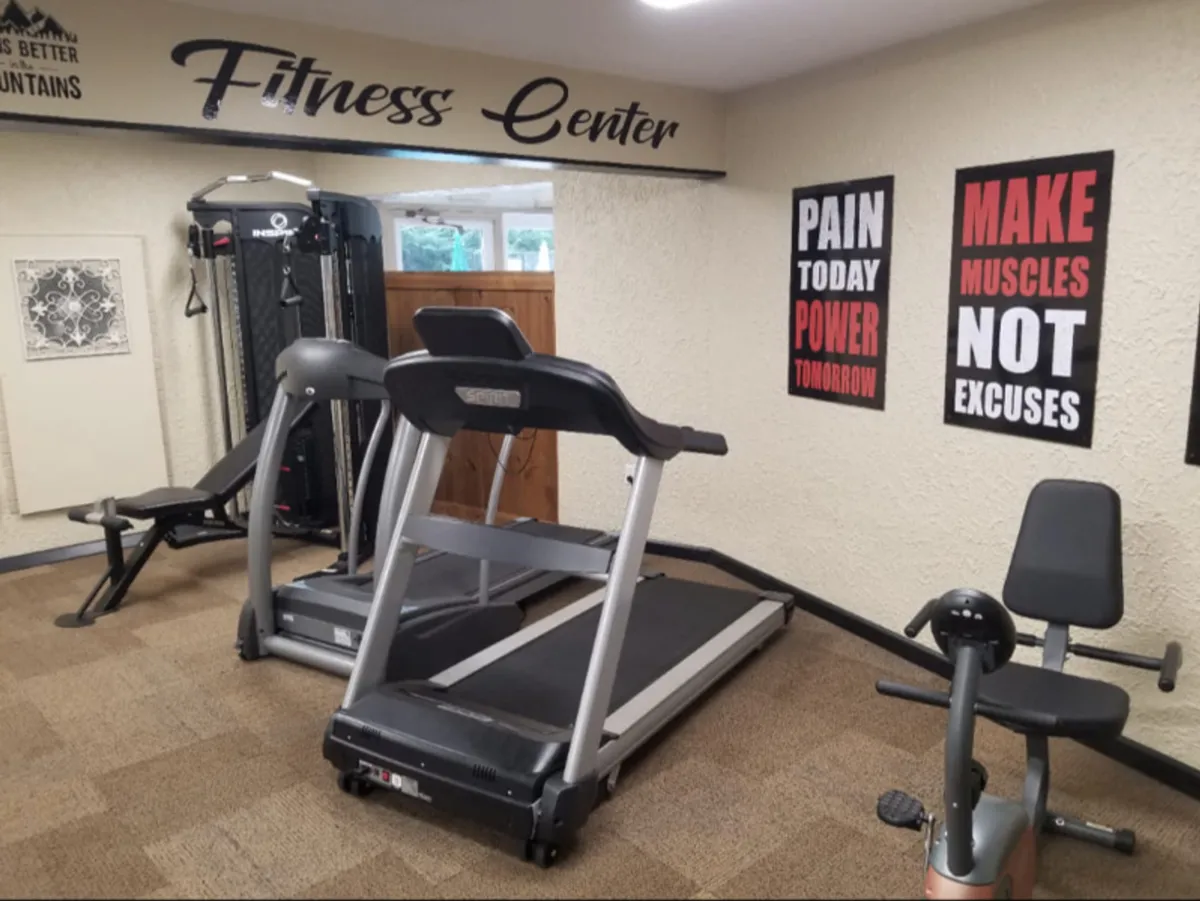 A bright, inviting fitness room equipped with treadmills and an exercise bike, featuring large windows and motivational posters on the walls. The space appears clean, modern, and energetic, ideal for starting the day with a revitalizing workout.